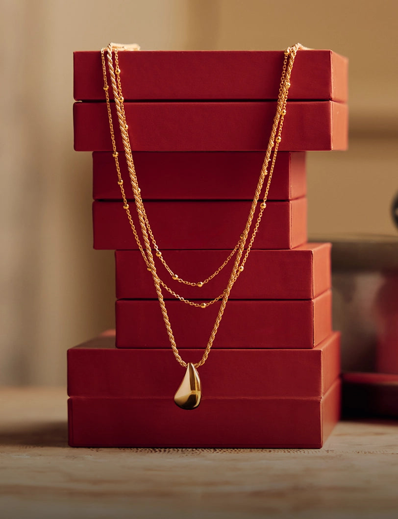 Gold tear drop necklace hanging from red jewellery boxes