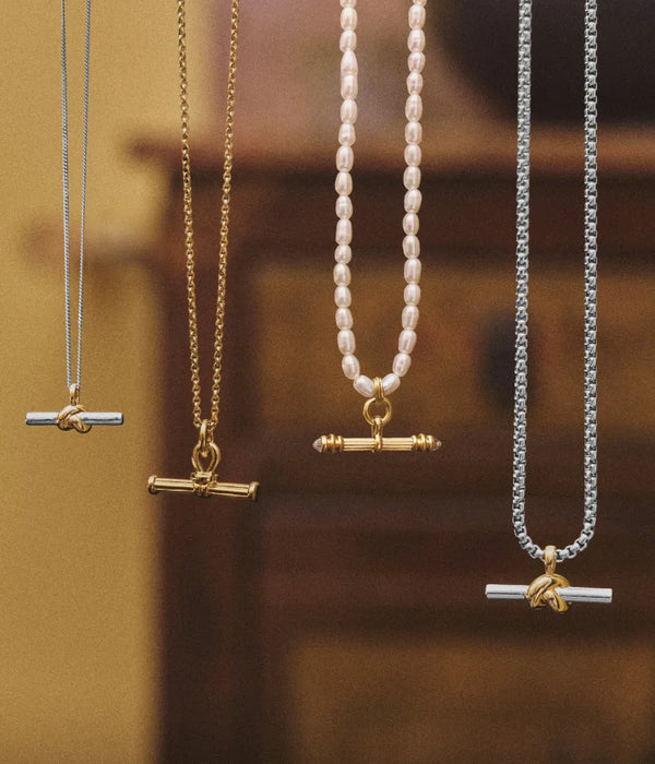 t-bar necklaces lined up. Lucy williams knot t-bar in gold and silver, ridge t-bar necklace in gold, harris reed pearl necklace with gold t-bar charm and lucy williams chunky t-bar necklace in gold and silver