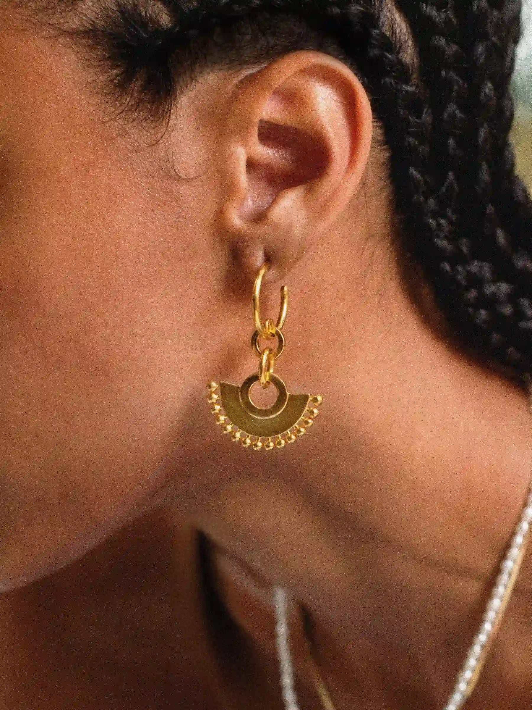 Close-up of a person wearing a gold hoop earring with a geometric design.