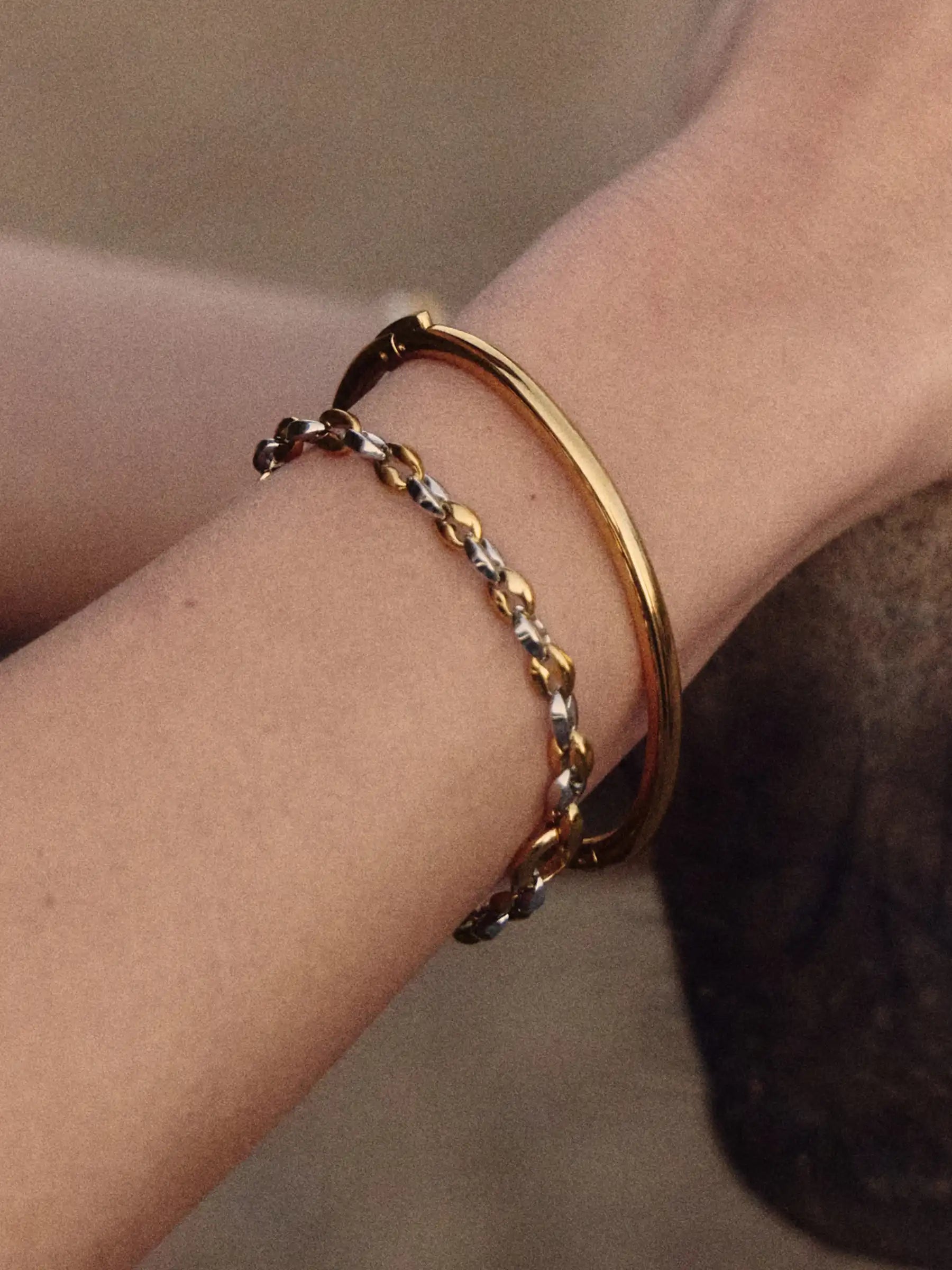 Gold and silver bracelets on a wrist against a neutral background