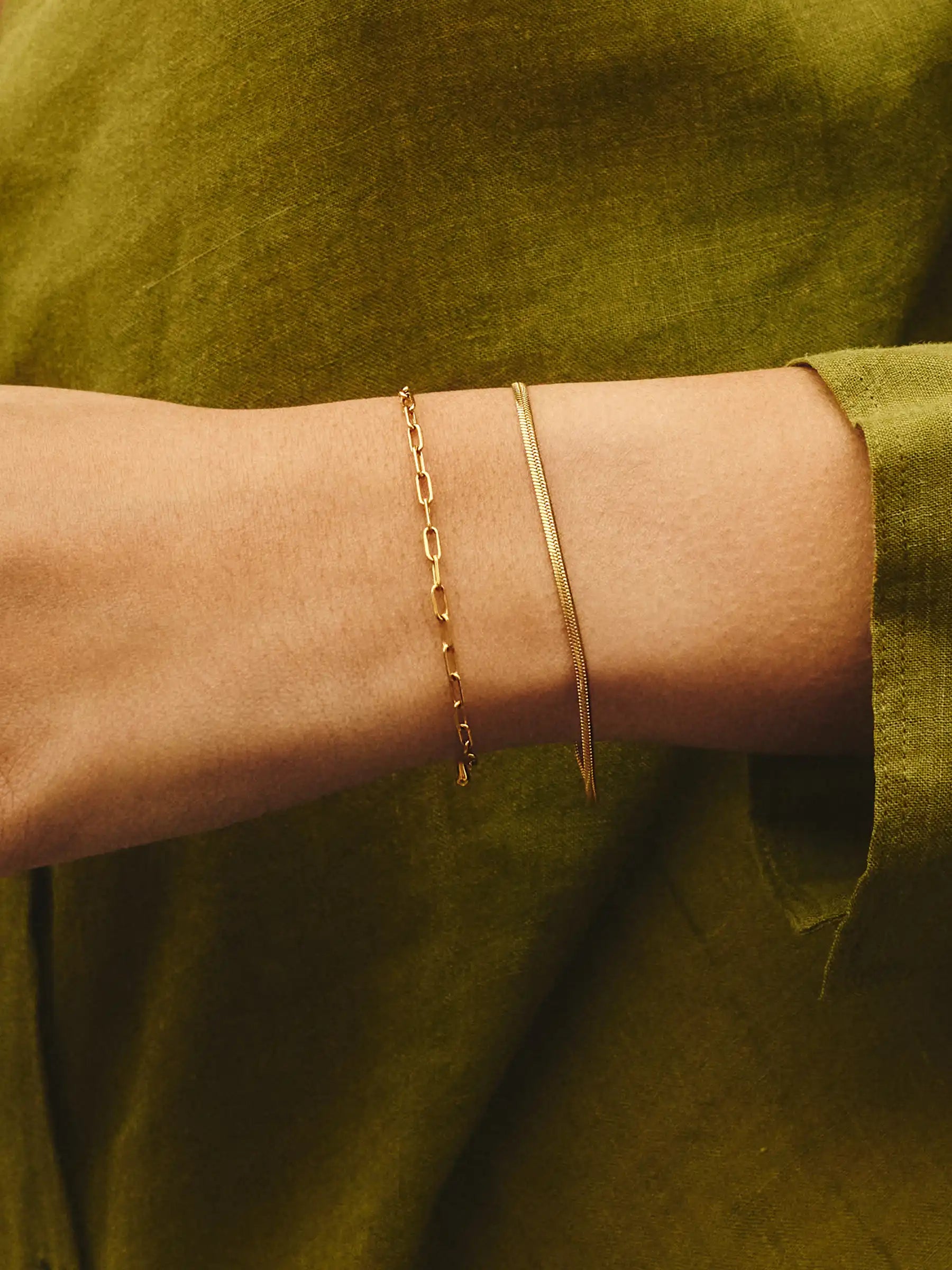 Gold bracelet on a wrist with a green background
